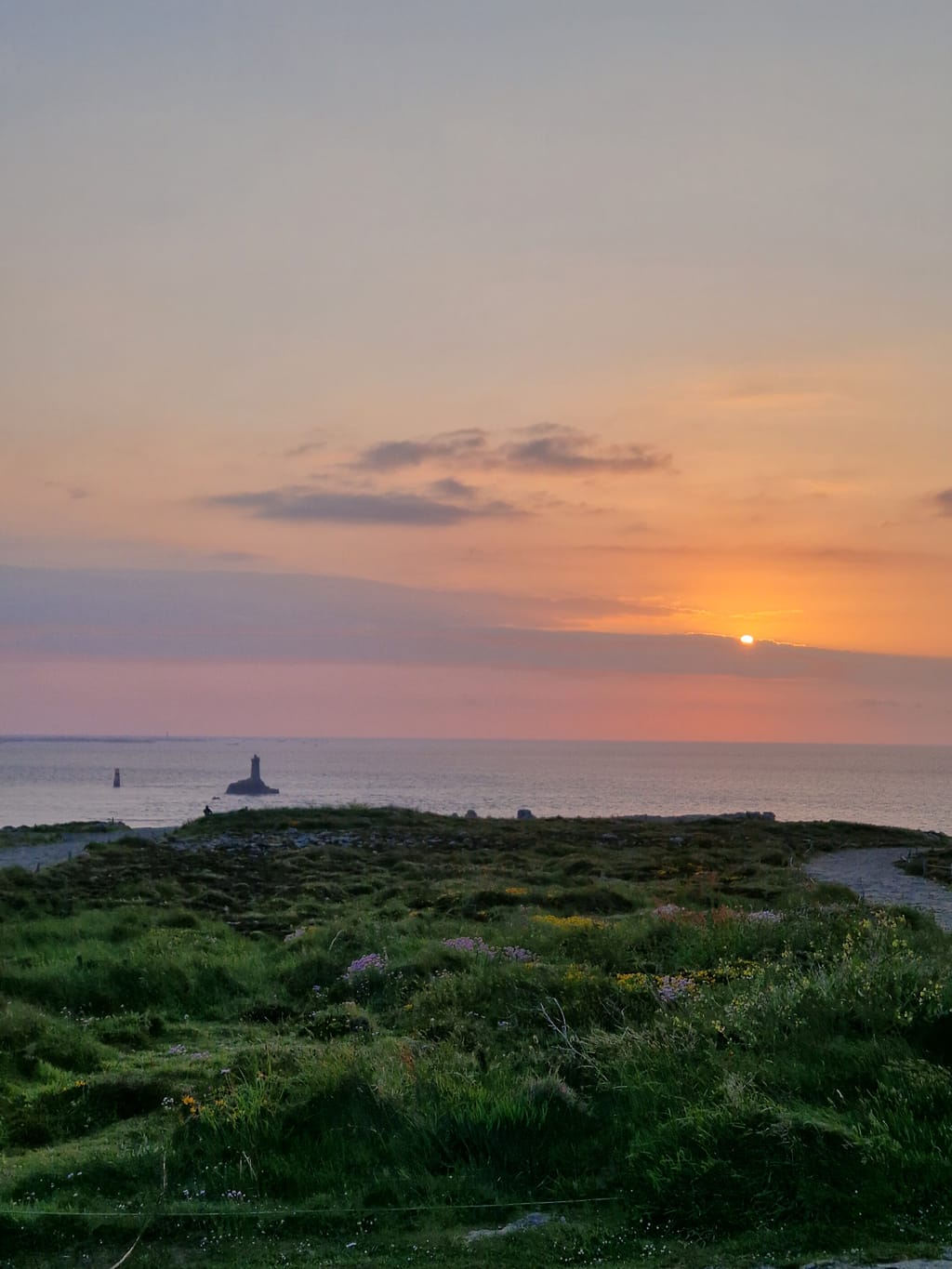 Il tramonto sull'oceano dalla brughiera di Pointe du Raz, con il faro all'orizzonte